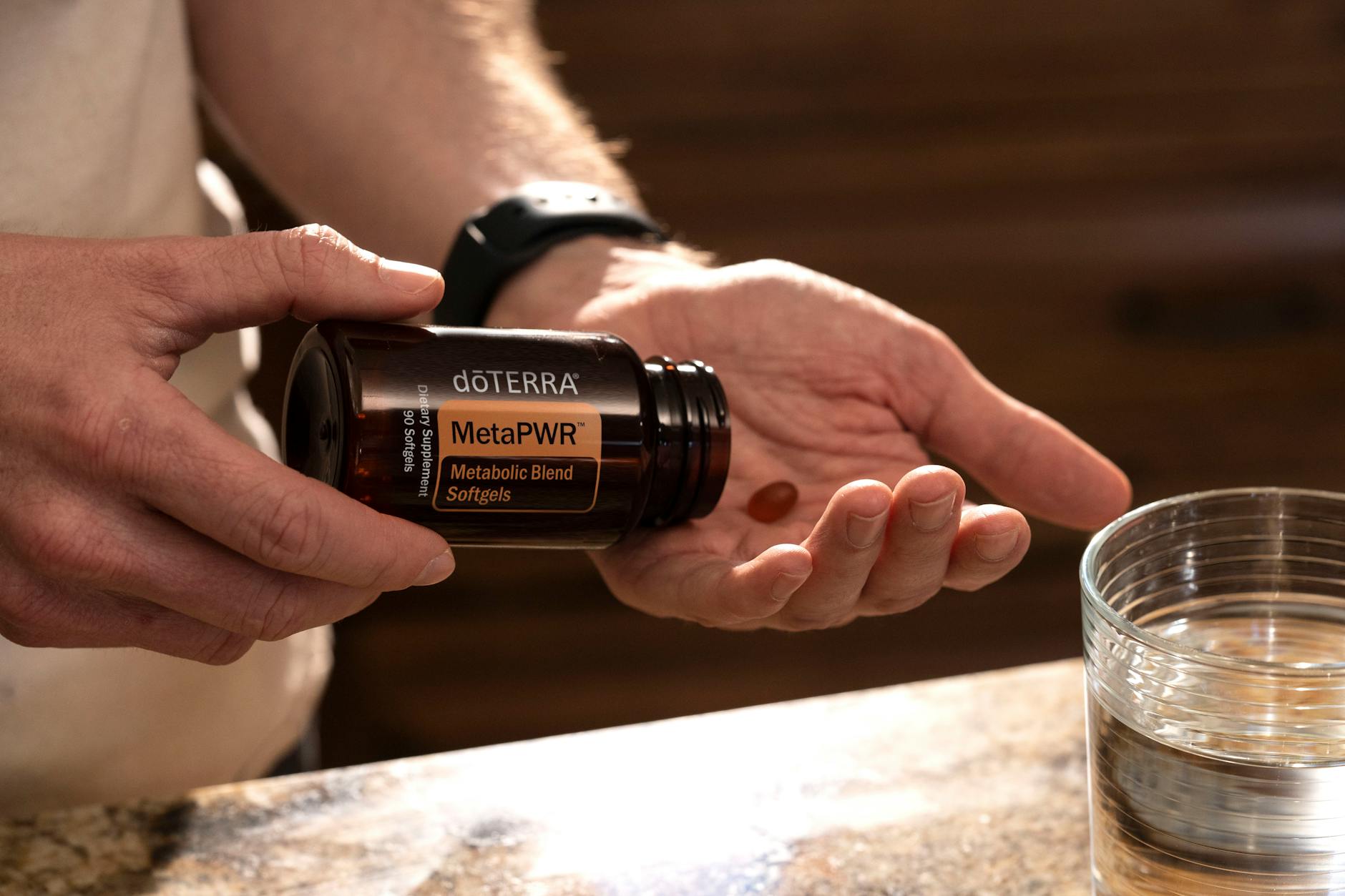 Hand holding MetaPWR metabolic blend softgels next to a glass of water. (Photo by doTERRA International, LLC on Pexels)