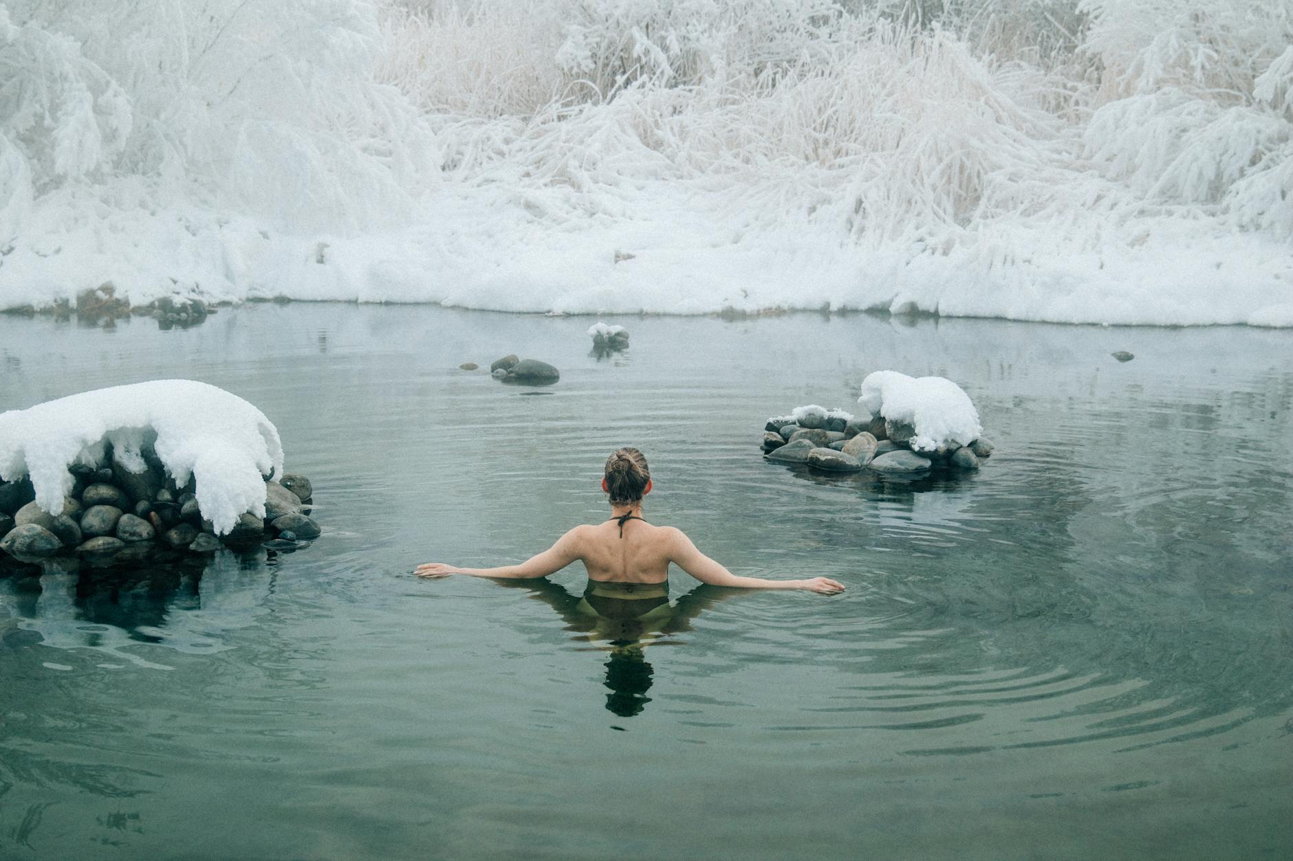 A young woman enjoying a swim in a tranquil winter lake surrounded by snow. (Photo by NIck Bulanov on Pexels)