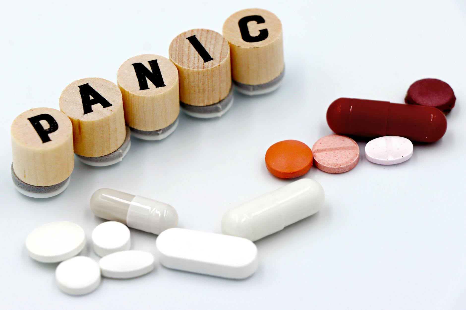 Assorted pills arranged beside wooden tiles spelling 'PANIC', symbolizing anxiety treatment. (Photo by Marta Branco on Pexels)