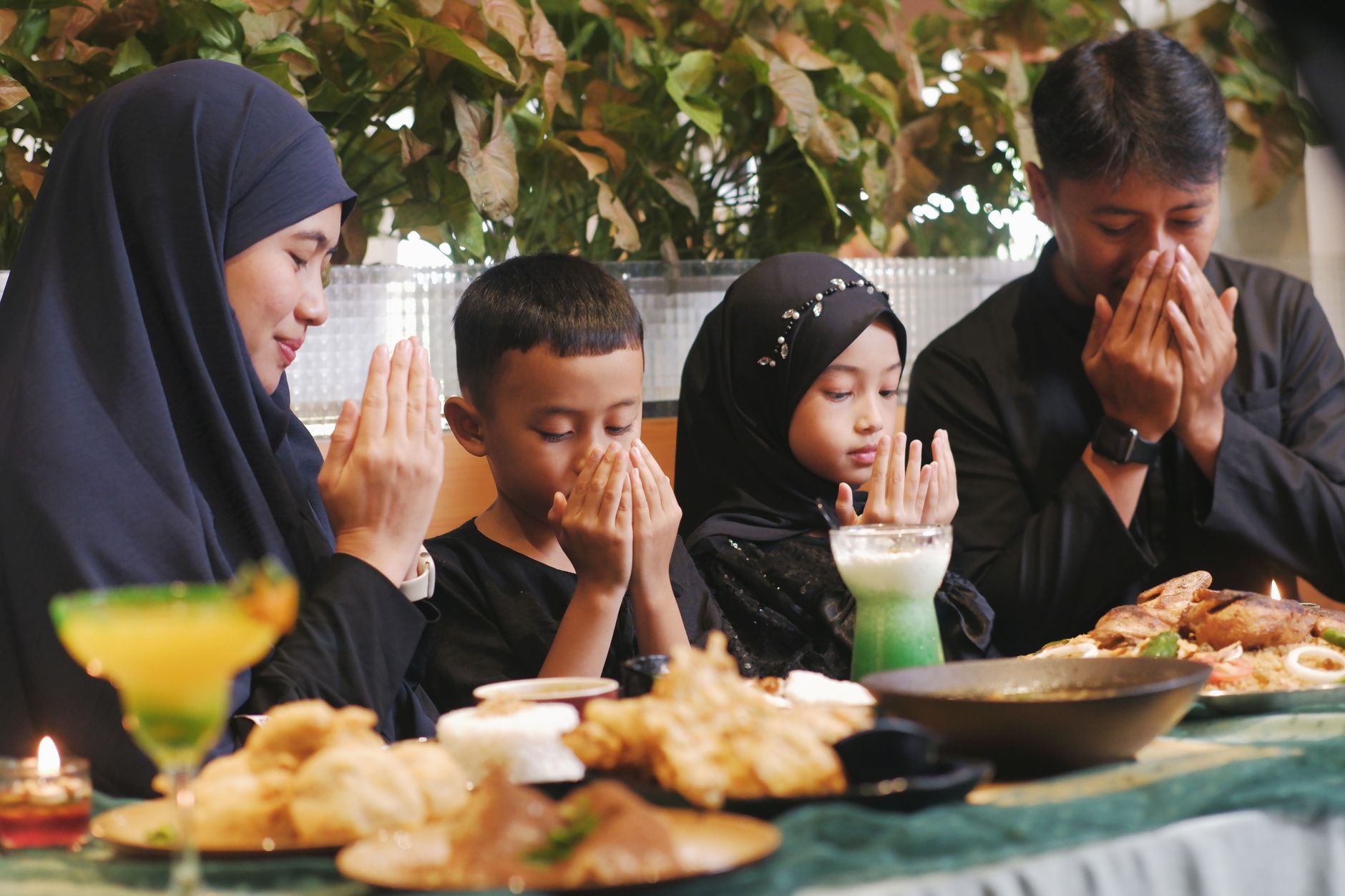 A family gathers indoors for a traditional Ramadan meal, praying together. (Photo by Nurul Sakinah Ridwan on Pexels)