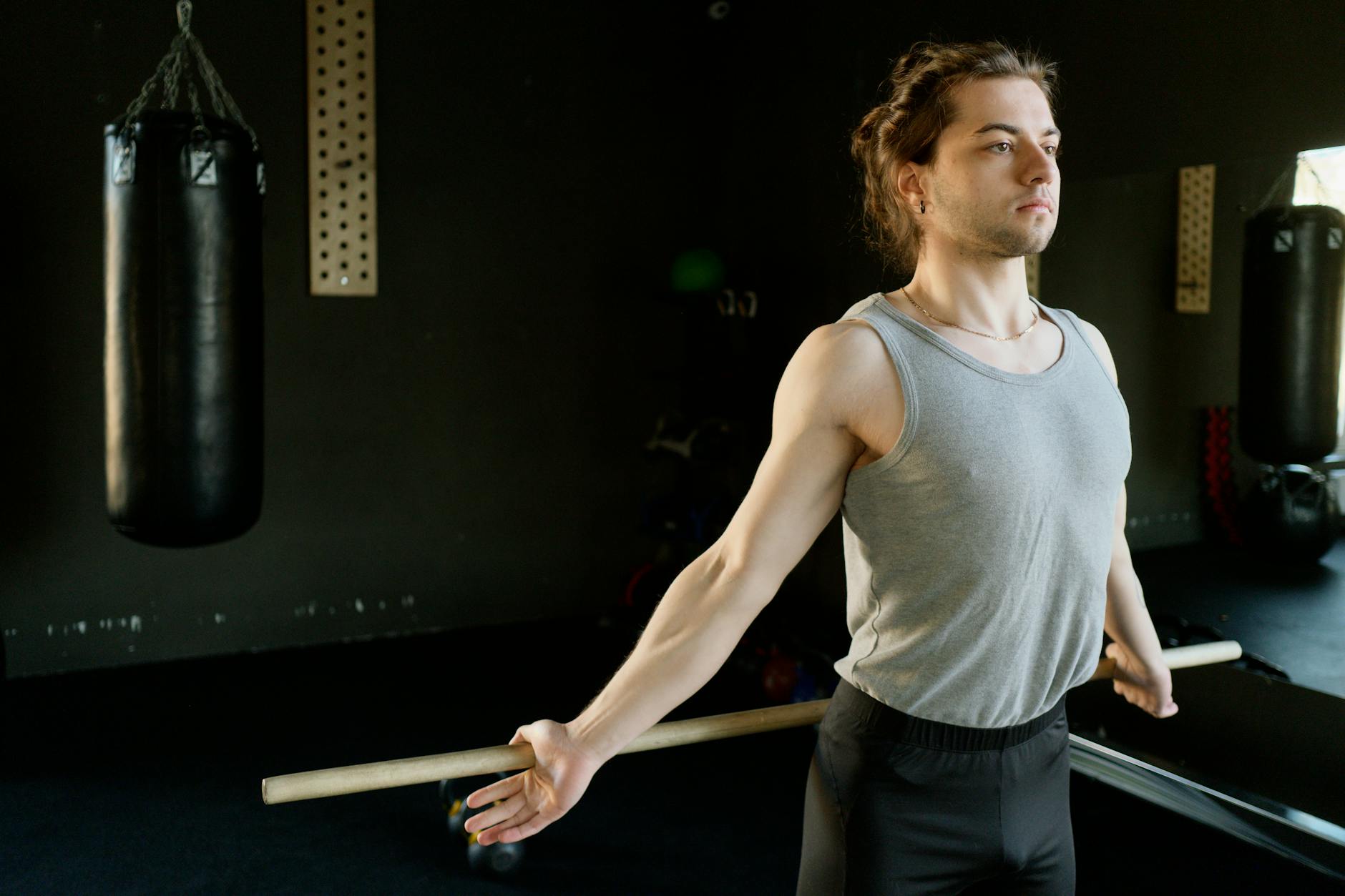 A man in a gym stretching with a rod next to a punching bag, emphasizing fitness and concentration. (Photo by Ivan S on Pexels)