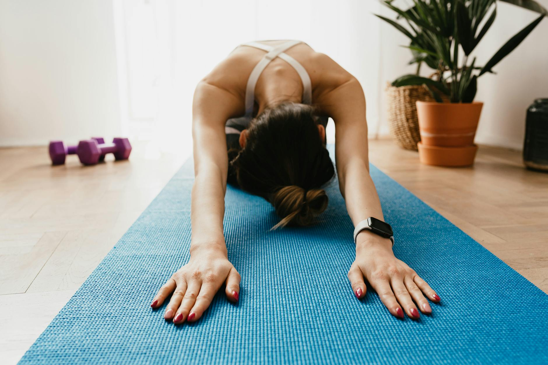 Full body faceless fit female wearing smartwatch stretching body in Child Pose on blue mat placed... (Photo by www.kaboompics.com on Pexels)