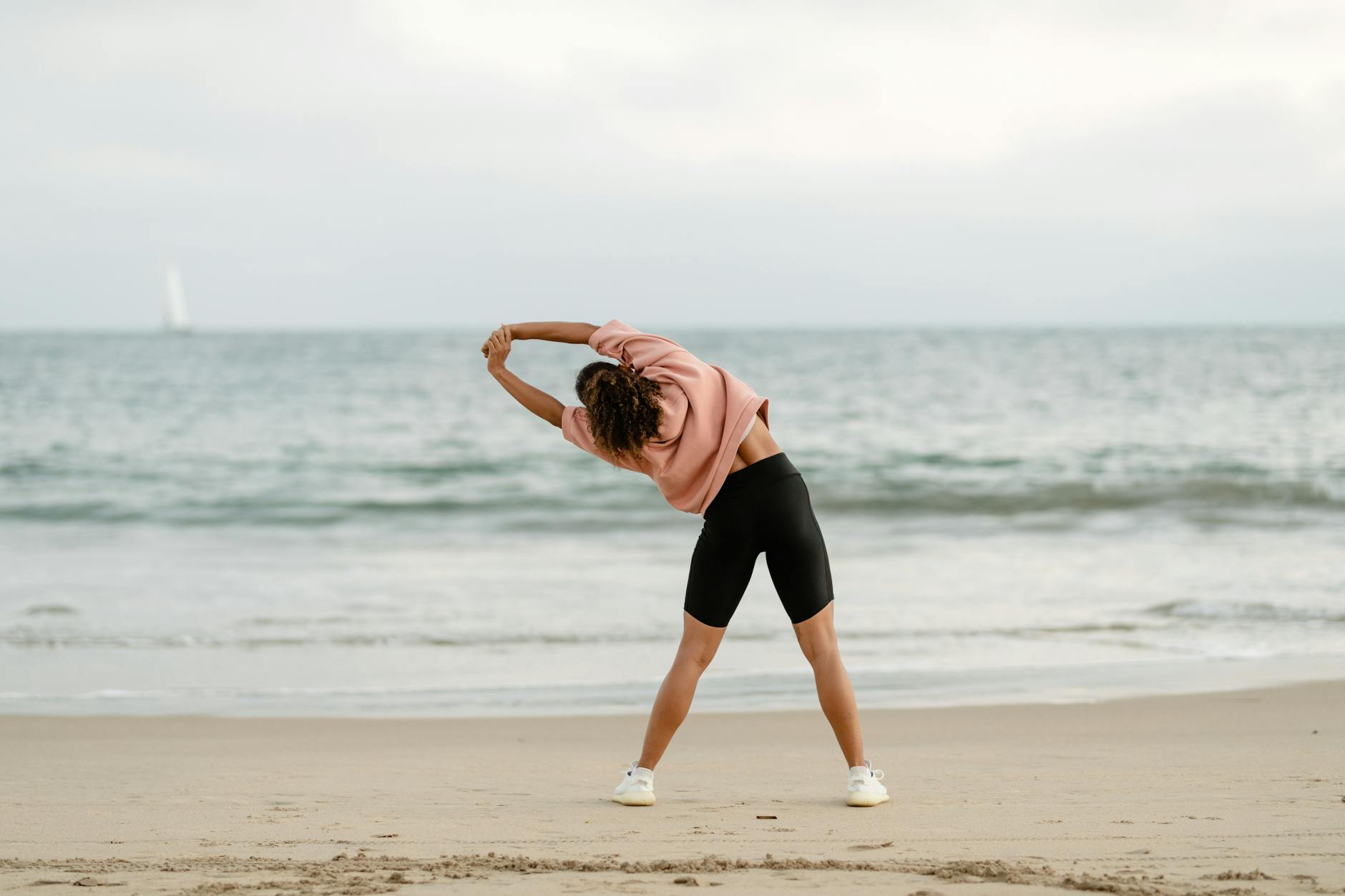 A woman stretching on the beach with a scenic ocean view at sunrise. (Photo by Ketut Subiyanto on Pexels)