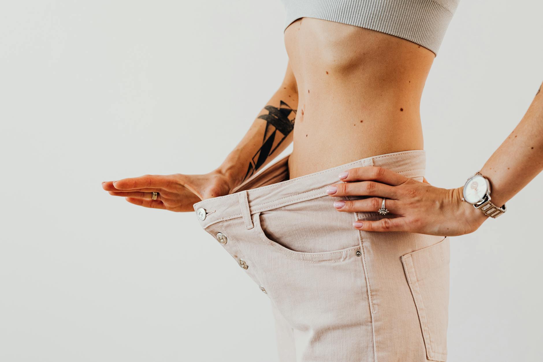 Close-up of a woman in oversized pants showcasing weight loss progress. Studio shot with neutral ... (Photo by www.kaboompics.com on Pexels)
