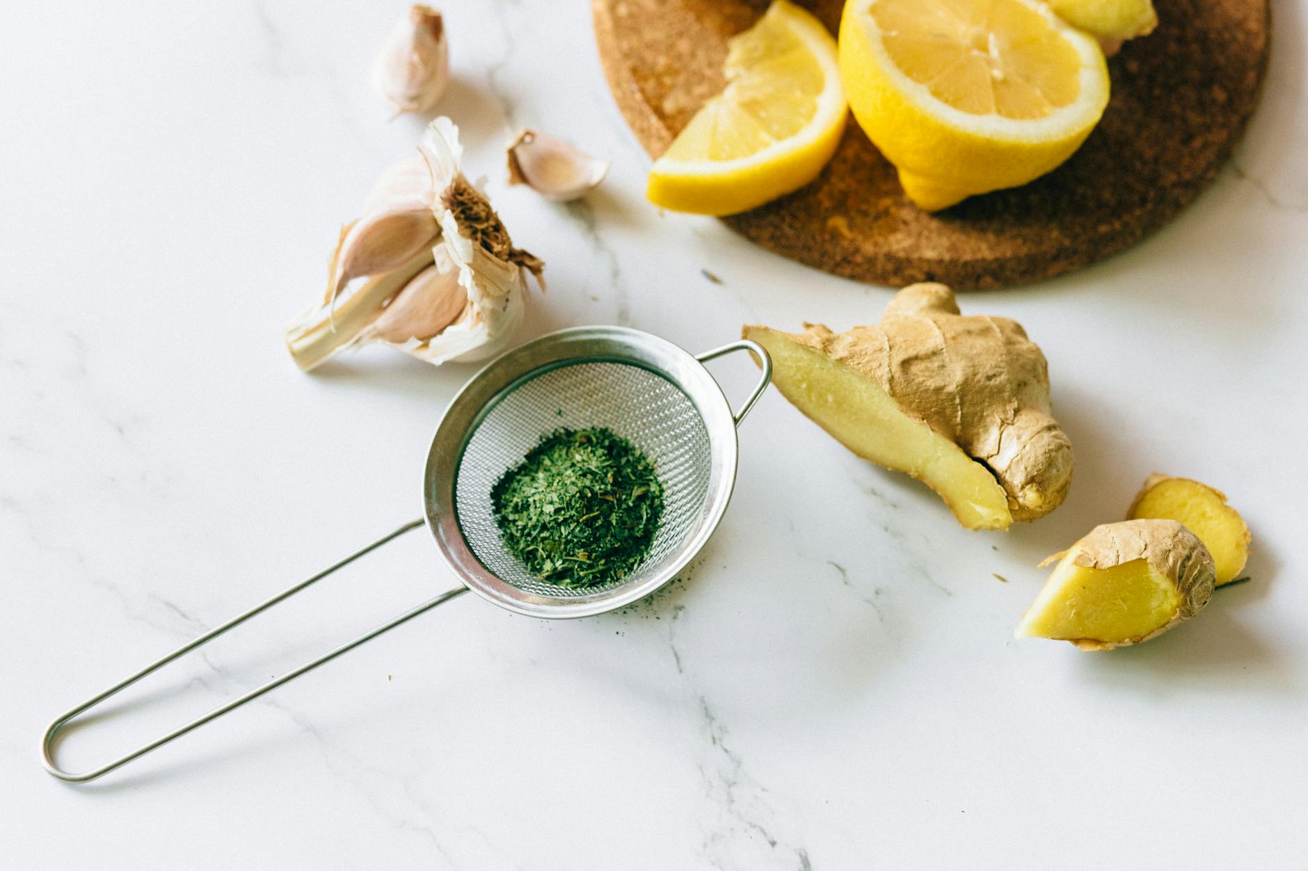 A flat lay of garlic, ginger, and lemon on a marble surface for natural remedies. (Photo by Nataliya Vaitkevich on Pexels)