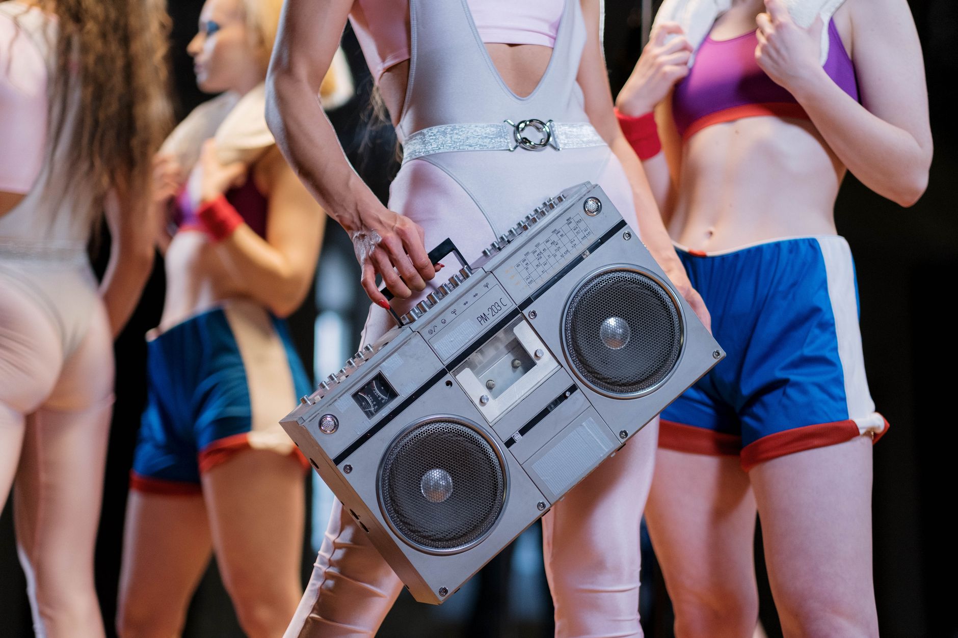 Group of women in retro workout clothes holding a vintage boombox indoors. (Photo by Ron Lach on Pexels)