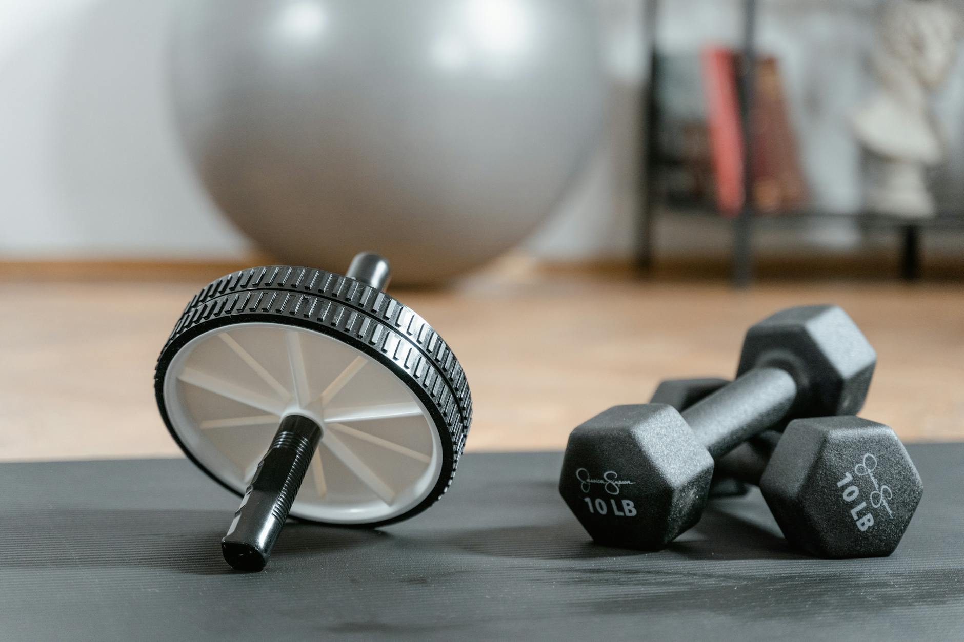 Close-up of ab wheel and dumbbells on a mat in a home gym setting. (Photo by MART  PRODUCTION on Pexels)