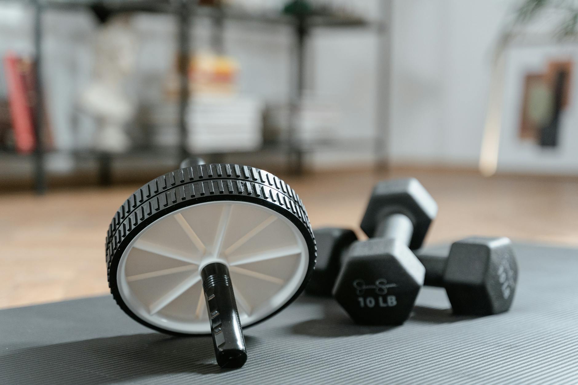 Ab roller and dumbbells on yoga mat, perfect for a home workout routine and healthy lifestyle. (Photo by MART  PRODUCTION on Pexels)