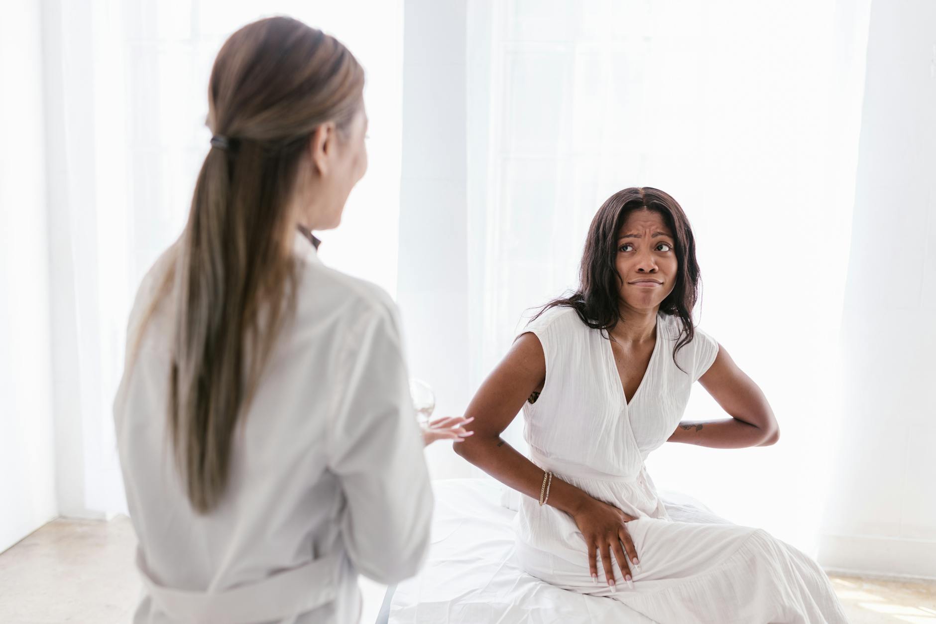 A woman with back pain consults her doctor in a clinical setting wearing a white dress. (Photo by RDNE Stock project on Pexels)