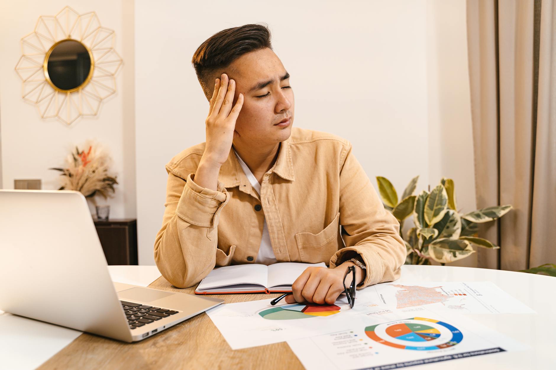 Businessman holding head in frustration, surrounded by documents and laptop at home office. (Photo by AI25.Studio  AI GENERATIVE on Pexels)