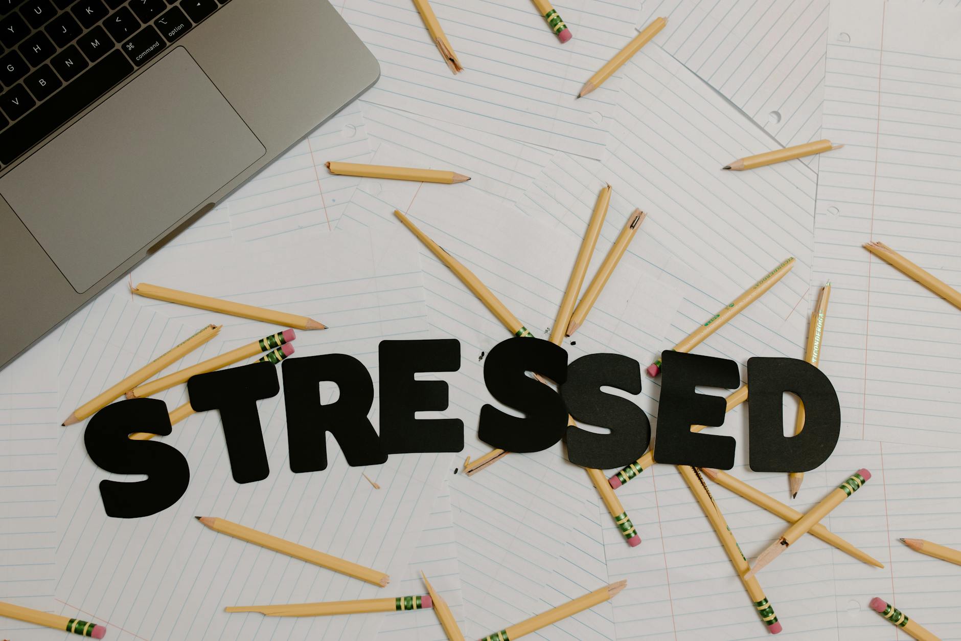 Overhead view of a stressed workplace setup with broken pencils scattered around a laptop. (Photo by Tara Winstead on Pexels)