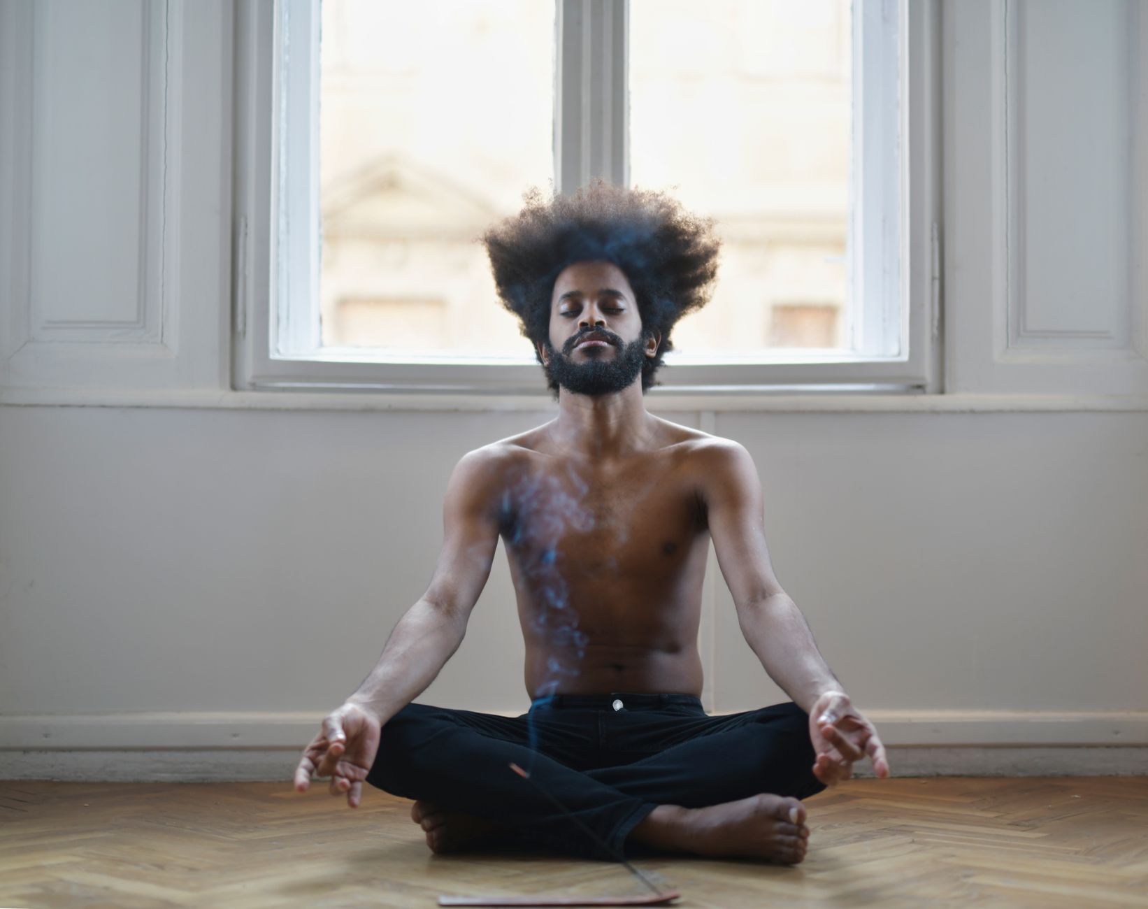 Shirtless man meditating on the floor, surrounded by soothing incense smoke in a tranquil room. (Photo by Andrea Piacquadio on Pexels)